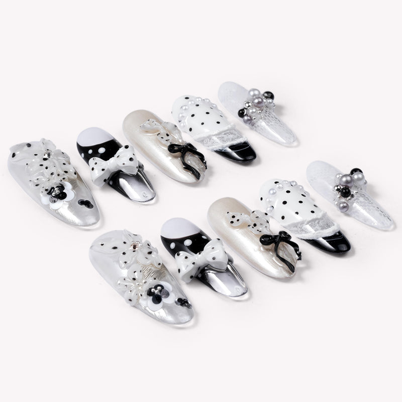 Flat lay of Coco Dot Affair press-on nails arranged in two rows with black and white polka dots, bows, lace, and pearl accents