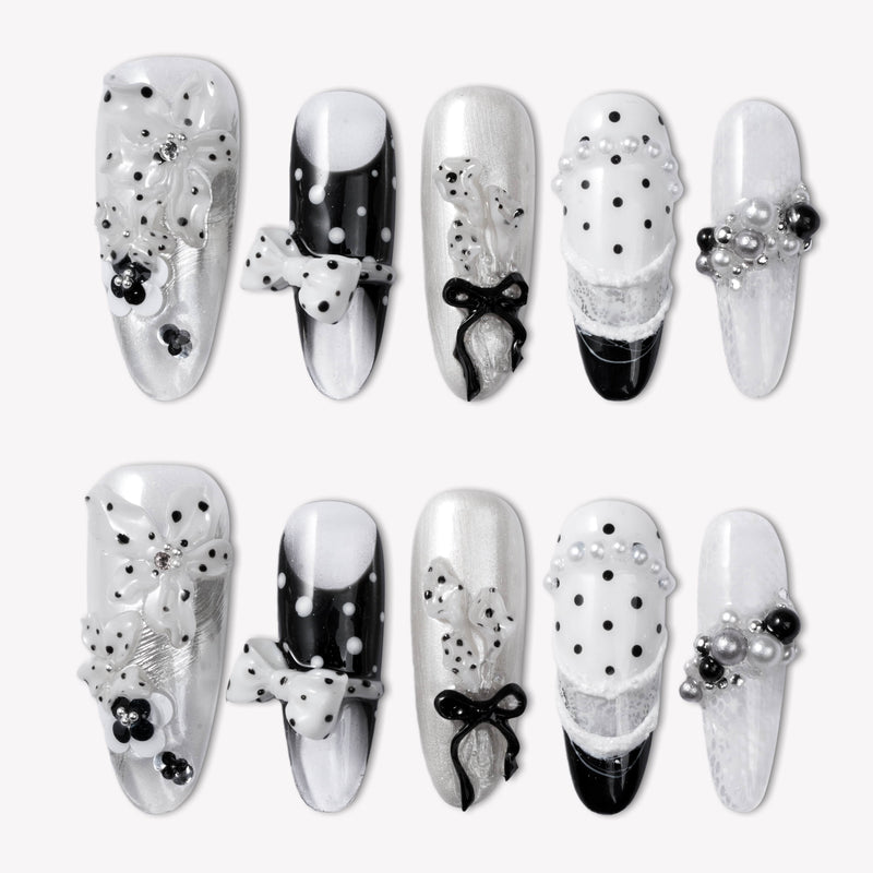 Flat lay of Coco Dot Affair press-on nails with black and white polka dots, bows, lace, and pearl accents