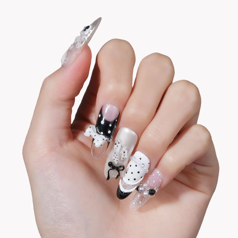 Hand model wearing Coco Dot Affair press-on nails with black and white polka dots, bows, lace, and pearl accents