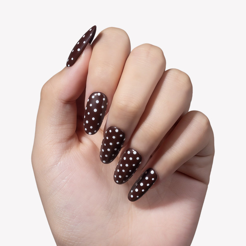 White background hand model wearing Cocoa Dots press-on nails with glossy dark brown bases and white polka dot accents