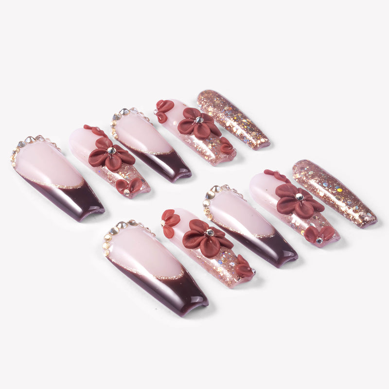 Angled flat lay of Coffee Blossom press-on nails with nude and brown French tips, 3D flowers, rhinestones, and rose gold glitter accents