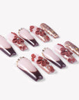 Angled flat lay of Coffee Blossom press-on nails with nude and brown French tips, 3D flowers, rhinestones, and rose gold glitter accents