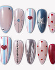 Cosmic Candy press-on nails with blue and white stripes, red heart charms, silver star accent, red polka dots, rhinestones, and glossy nude bases