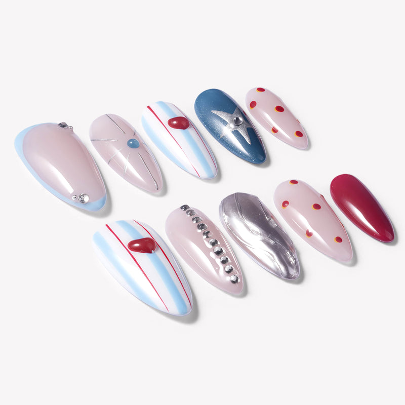 Flat lay of Cosmic Candy press-on nails with blue and white stripes, red heart charms, silver star accent, red polka dots, rhinestones, and silver cat eye design