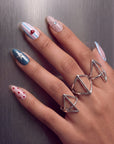 Hand model wearing Cosmic Candy press-on nails with blue and white stripes, red heart charm, silver star accent, red polka dots, rhinestones, and silver rings