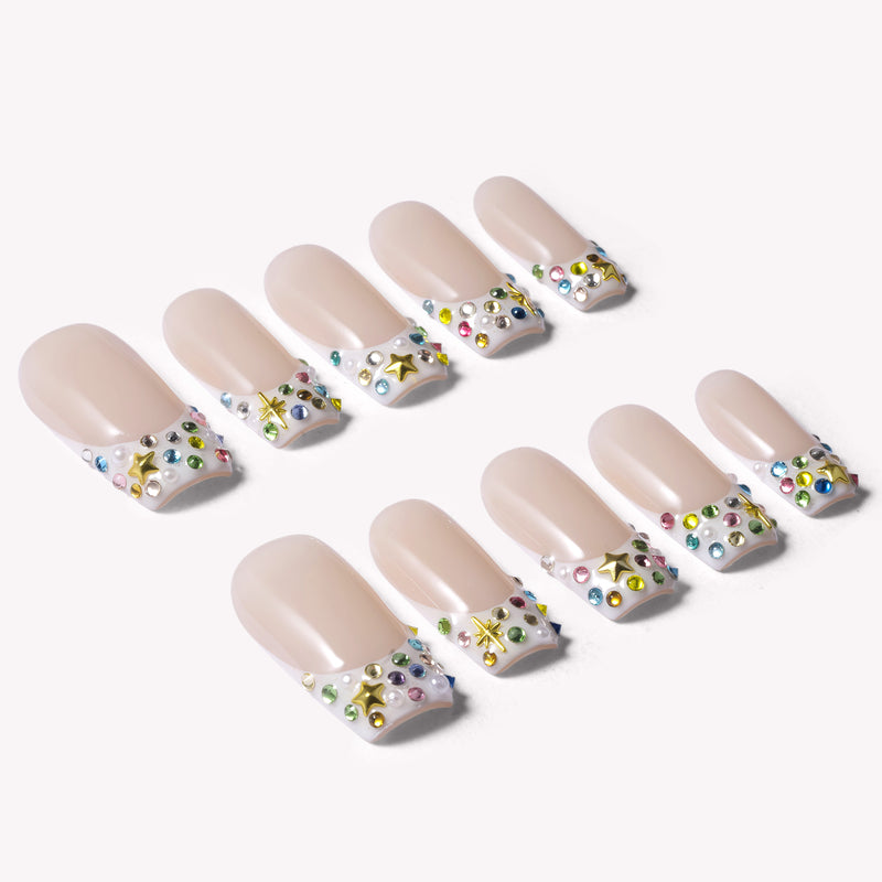 Full set of nude French tip press-on nails with multicolor rhinestones, iridescent pearls and gold star charms on white background