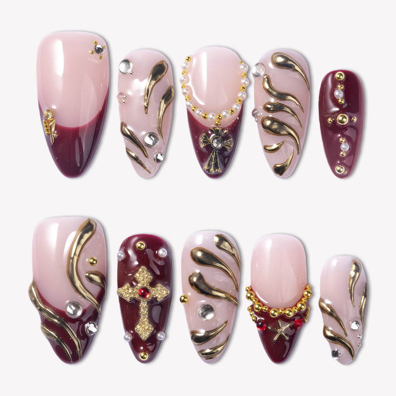 Flat lay of pale pink and burgundy press-on nails with gold swirls, crystals, and cross embellishments.