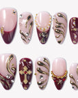 Flat lay of pale pink and burgundy press-on nails with gold swirls, crystals, and cross embellishments.