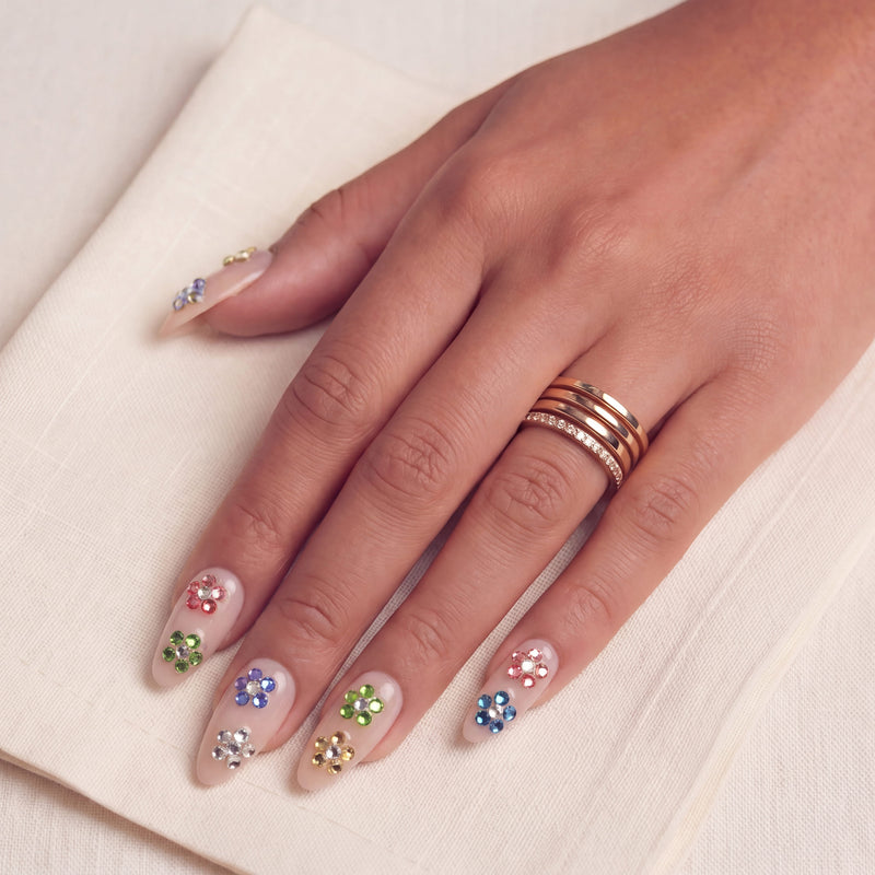 Crystal Dew handmade press on nails worn on a hand model with colorful rhinestone accents on a cream fabric background