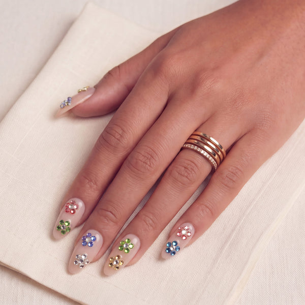 Crystal Dew handmade press on nails worn on a hand model with colorful rhinestone accents on a cream fabric background
