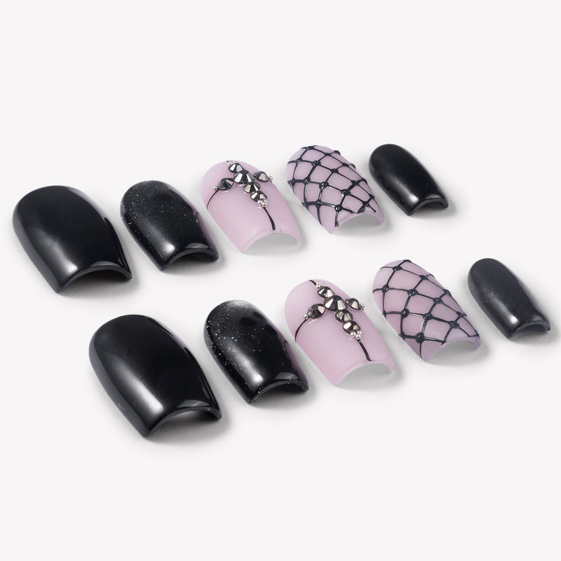 Angled flat lay of Dark Masquerade press-on nails with glossy black finishes, pink rhinestone cross accents, black glitter, and raised fishnet designs