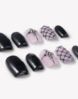 Angled flat lay of Dark Masquerade press-on nails with glossy black finishes, pink rhinestone cross accents, black glitter, and raised fishnet designs