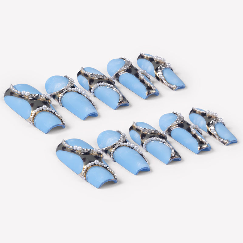 Angled flat lay of Denim Luxe press-on nails with sky blue bases, gold black leopard accents, pearl chains, and rhinestone details