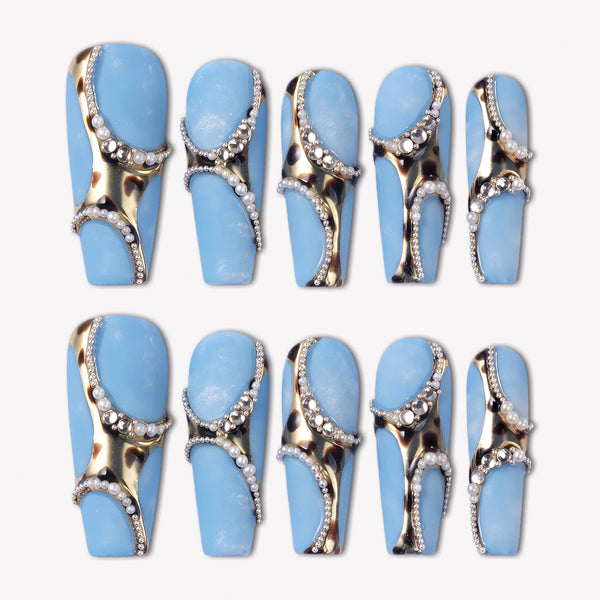 Denim Luxe press-on nails with sky blue bases, gold and black leopard accents, pearl chains, and rhinestone details