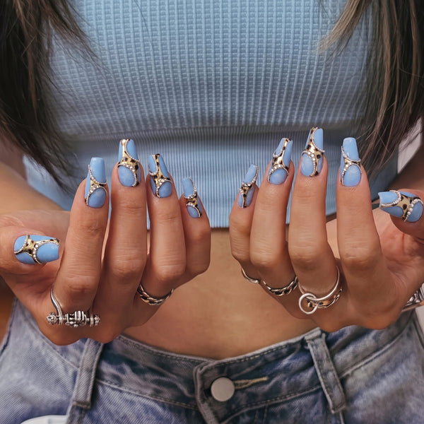 Hand model wearing Denim Luxe press-on nails with sky blue bases, gold and black leopard accents, pearl chains, and rhinestones