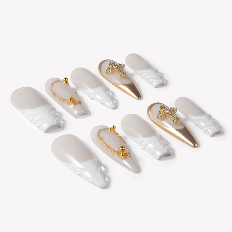 Angled flat lay of Divine Grace press-on nails with white sculpted bases, nude pearl shimmer, gold chrome accents, bead details, and rhinestone crosses