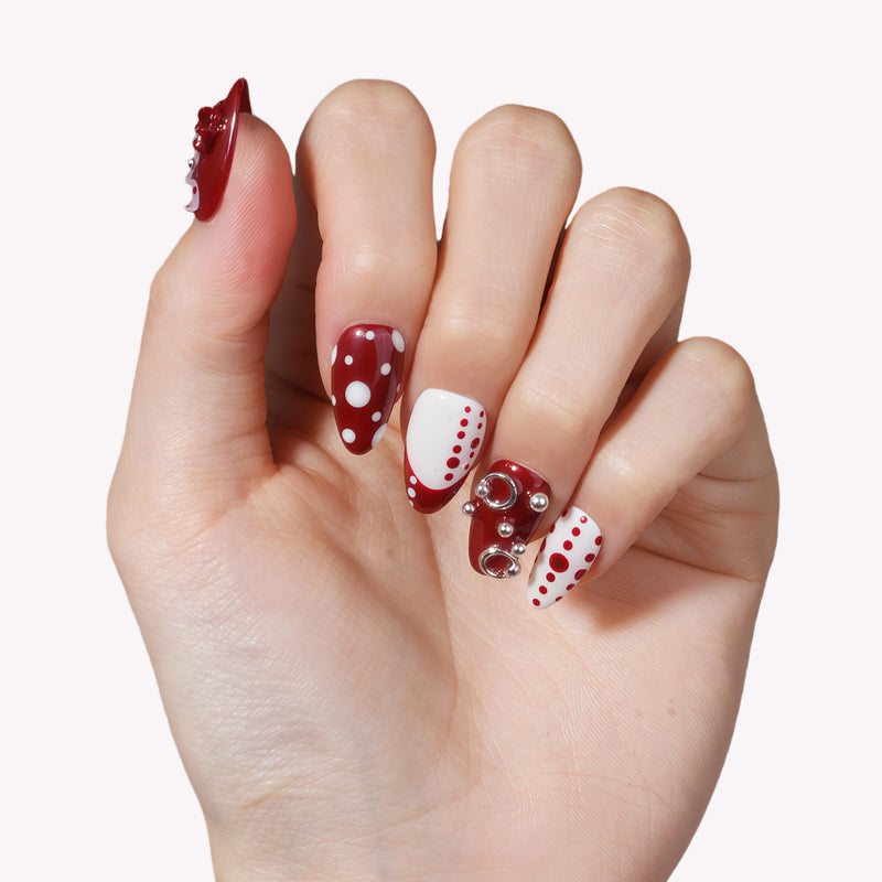 Hand model wearing Dot Fantasy press-on nails in red and white with polka dots and jeweled 3D accents