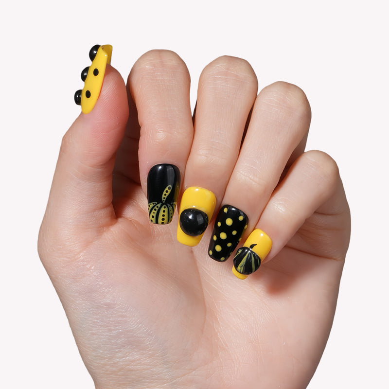Hand model wearing Dot Obsession press-on nails in black and yellow with bold polka dots