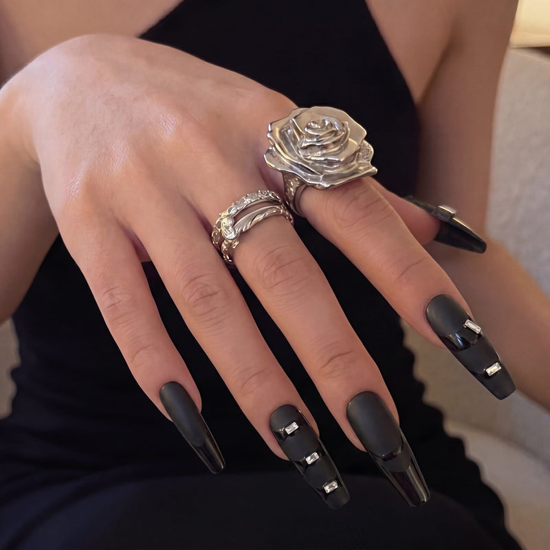 Hand model wearing Eclipse Luxe press-on nails with black matte and glossy panels, rectangular rhinestones, and silver rose ring styling