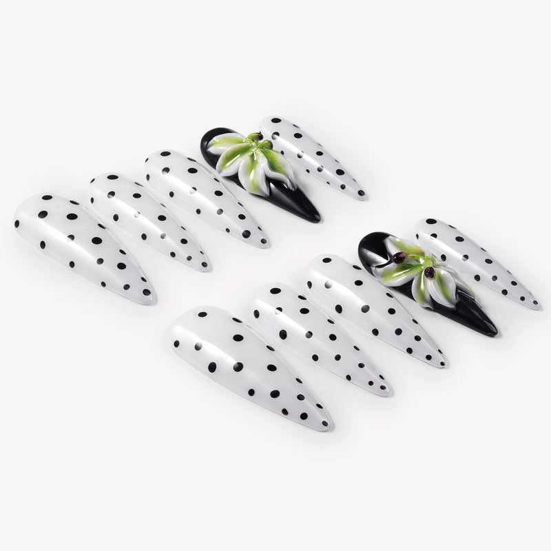 Flat lay of Eden Polka press-on nails with white bases, black polka dots, glossy black accent nails, and raised green white flower designs