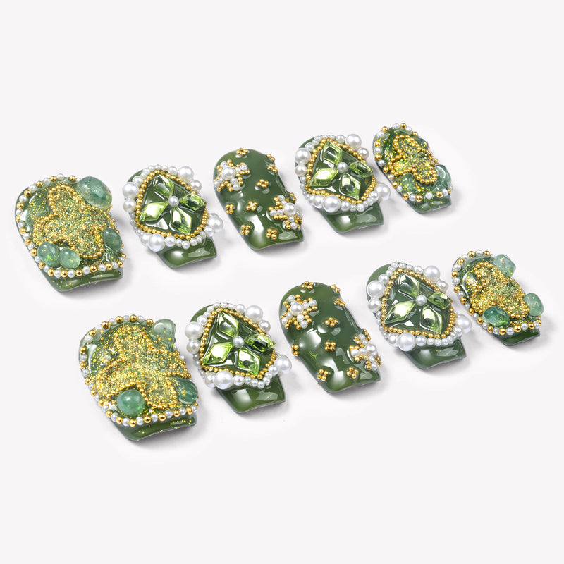 Angled flat lay of Emerald Crown press-on nails with glossy green bases, faceted green gems, pearl borders, and gold bead accents