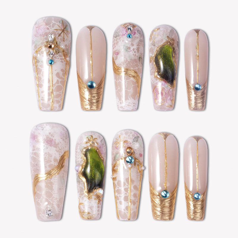 Enchanted Garden press-on nails with pale pink bases, raised gold linework, blue rhinestones, pearl accents, and green gemstone charms