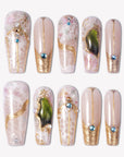Enchanted Garden press-on nails with pale pink bases, raised gold linework, blue rhinestones, pearl accents, and green gemstone charms