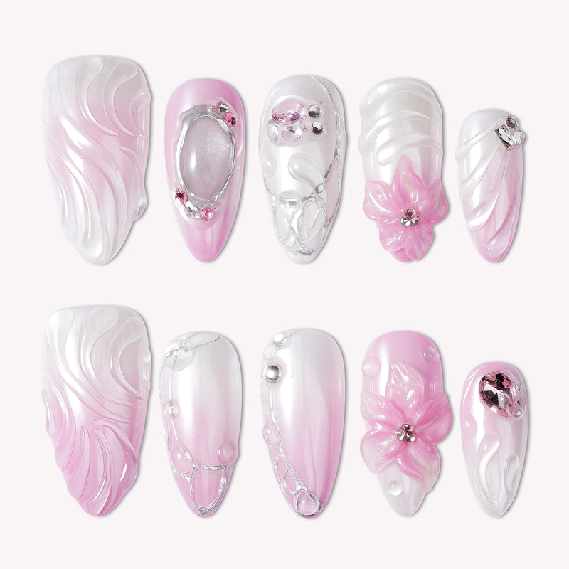 Pink and white ombré press-on nails with 3D floral and gem accents arranged in a flat lay
