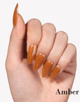 Hand model wearing Fall Essence Amber press-on nails in a glossy amber orange brown shade with almond-shaped tips
