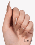 Hand model wearing Fall Essence Latte press-on nails in a warm caramel brown shade with glossy almond-shaped tips
