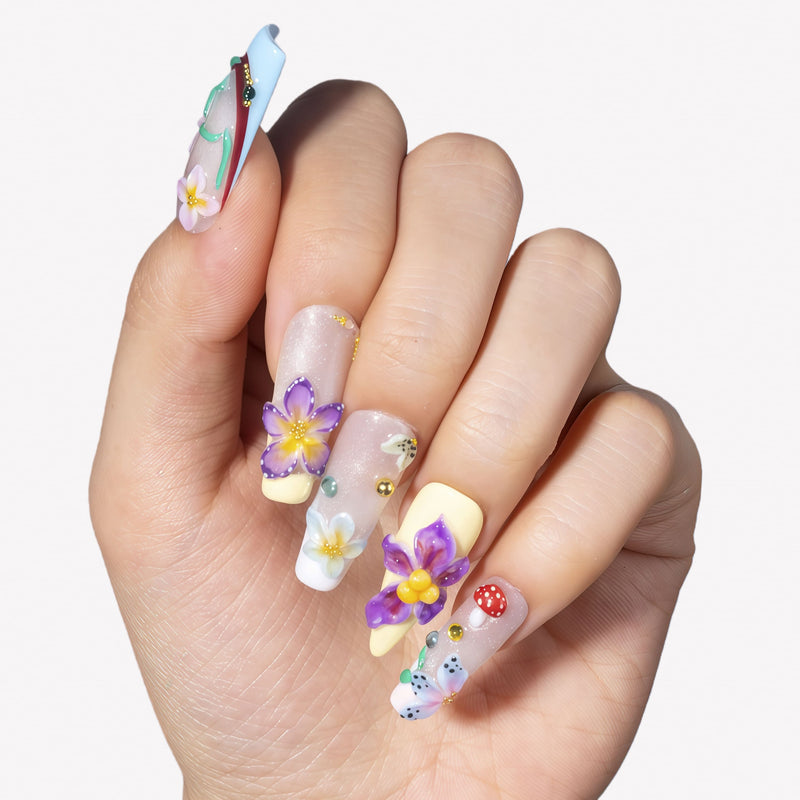 Hand model wearing Floral Symphony press-on nails with 3D purple flowers, white blossoms, mushrooms, and rhinestones