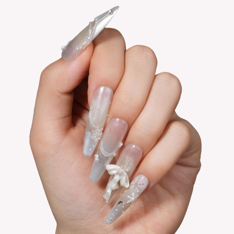 Close-up of a hand model wearing Frosted Ballet press-on nails with translucent silver shimmer, snowflake accents, and ribbon bows