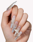 Close-up of a hand model wearing Frosted Ballet press-on nails with translucent silver shimmer, snowflake accents, and ribbon bows