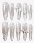 Flat lay of Frosted Ballet press-on nail swatches with pearl white and silver shimmer finishes, snowflake accents, and ribbon bows