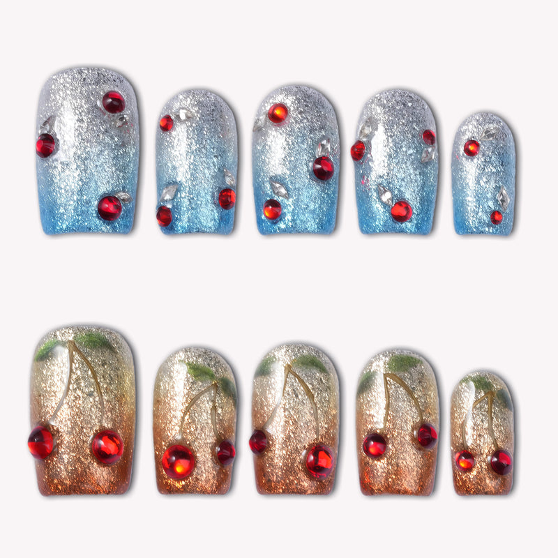 Frosted Cherry press-on nails in silver blue and gold ombre with red gem accents arranged on a white background