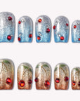 Frosted Cherry press-on nails in silver blue and gold ombre with red gem accents arranged on a white background