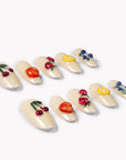 Angled flat lay of Fruit Crush glossy cream press-on nails with colorful raised cherry, peach, berry, and lemon designs