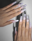 Flat hand model view of Ghosted Love square press-on nails with pink ombre bases, white spider webs, ghost faces, and silver rhinestone clusters