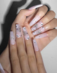 Overlapped hands wearing Ghosted Love press-on nails with pink bases, white spider webs, ghost faces, silver rhinestone clusters, and heart charms