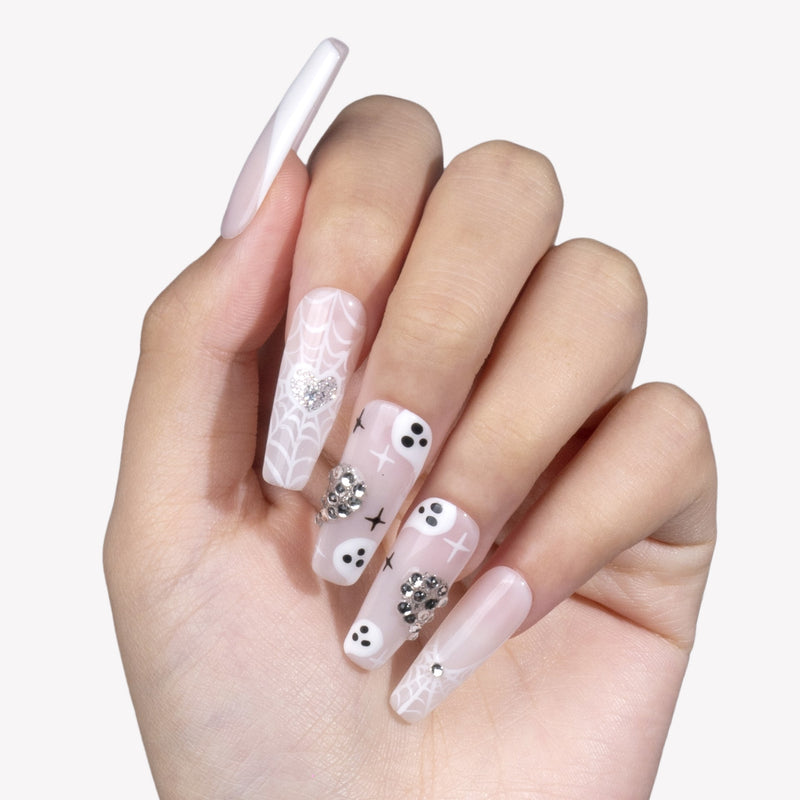 White background hand model wearing Ghosted Love press-on nails with pale pink bases, white spider webs, ghost faces, and silver rhinestone details