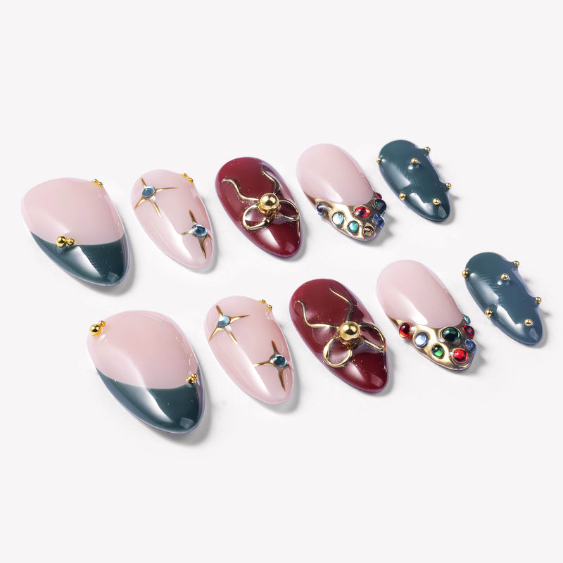 Angled flat lay of Gilded Noel press-on nails with burgundy, deep teal, nude pink, gold bow, pearls, and jewel accents