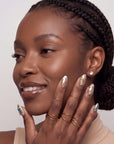 A hand model wearing champagne shimmer press-on nails with butterfly details, pearls, and rhinestones