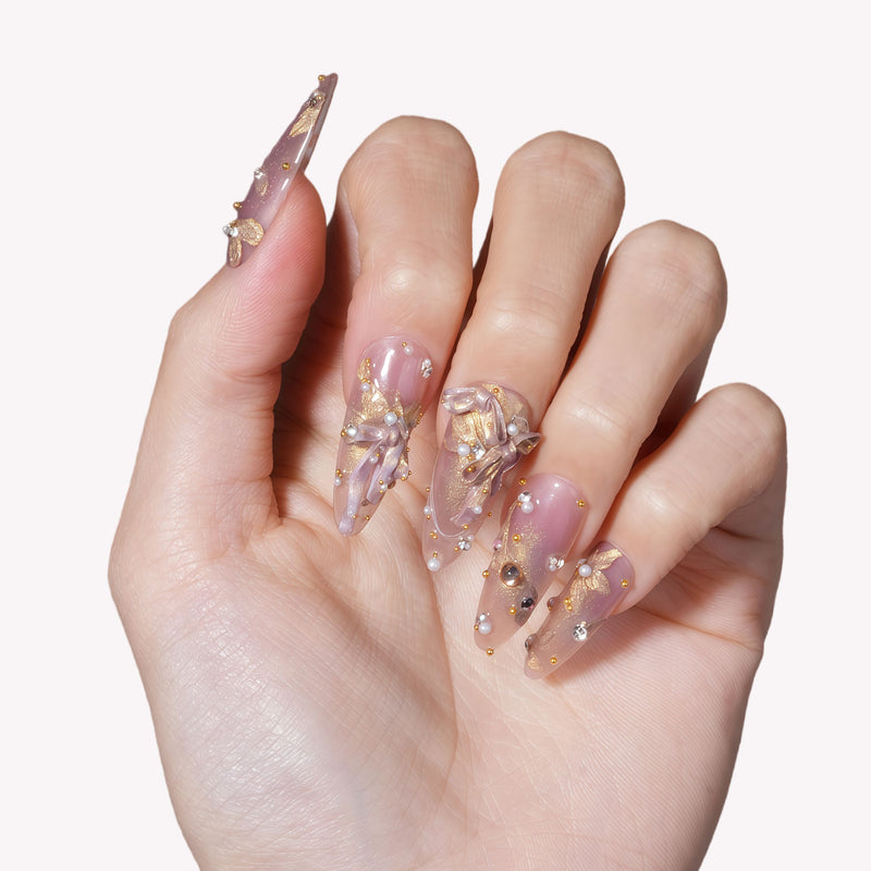 Close-up of a hand model wearing Gilded Petal Waltz press-on nails in soft lavender and gold with floral accents, pearls, and rhinestones