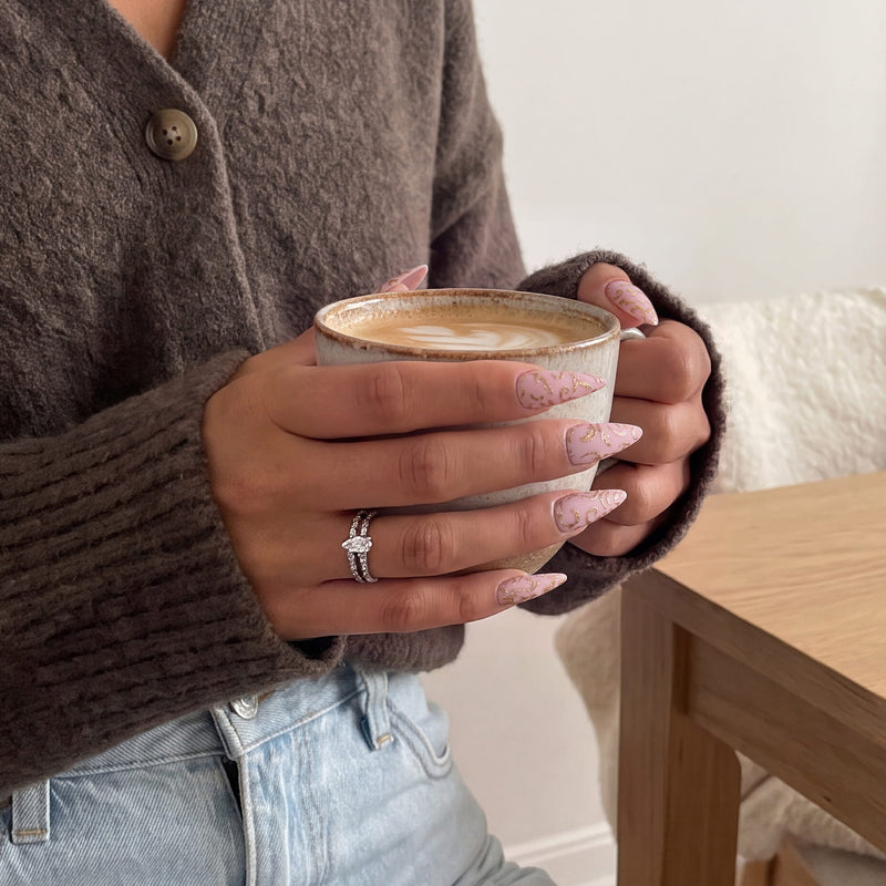 Hand model holding a coffee cup while wearing Gilded Petals press-on nails with pink bases and raised gold vine patterns
