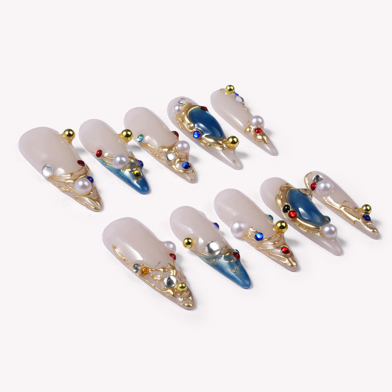 Flat lay of Gilded Relic Blue press-on nail swatches with blue gems, pearls, and gold accents
