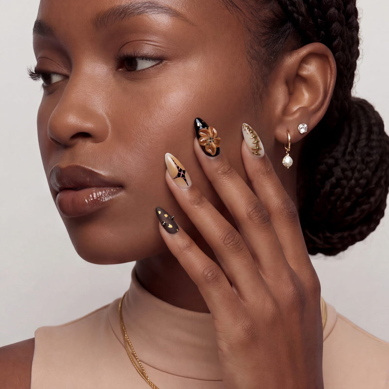 A hand model wearing warm brown and gold press-on nails poses beside the face in a close-up portrait.