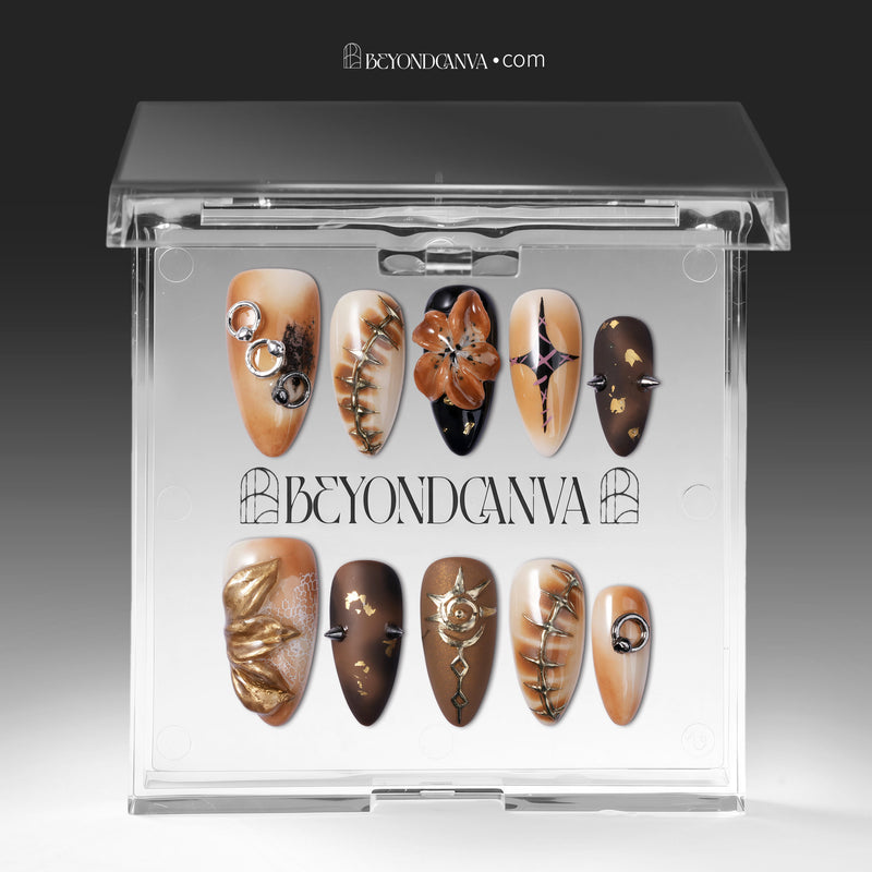 A clear display box shows brown and gold press-on nails with metallic rings, spikes, florals, and abstract accents.