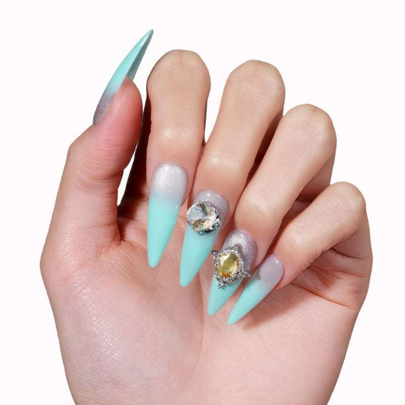 Hand model wearing Glacier Jewel press-on nails with icy blue ombré, a large crystal accent, and yellow jewel embellishments