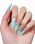 Hand model wearing Glacier Jewel press-on nails with icy blue ombré, a large crystal accent, and yellow jewel embellishments