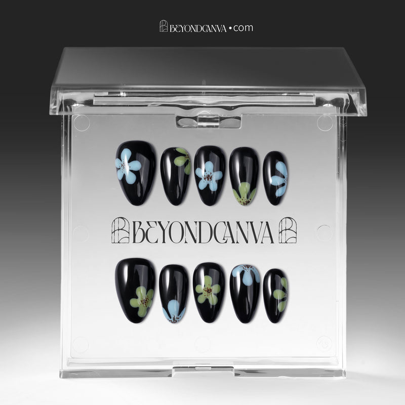 A transparent display case shows black press-on nails with blue and green flower accents arranged in two rows.